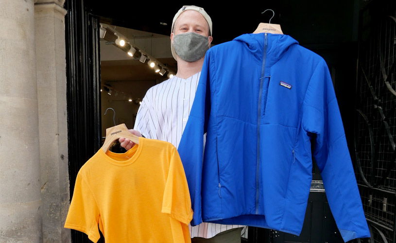 Patagonia sales person in mask holding up clothes for sale.